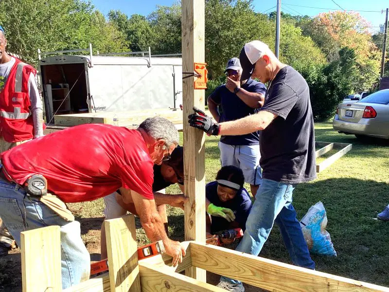 Group of men building a wooden structure outdoors on a sunny day.