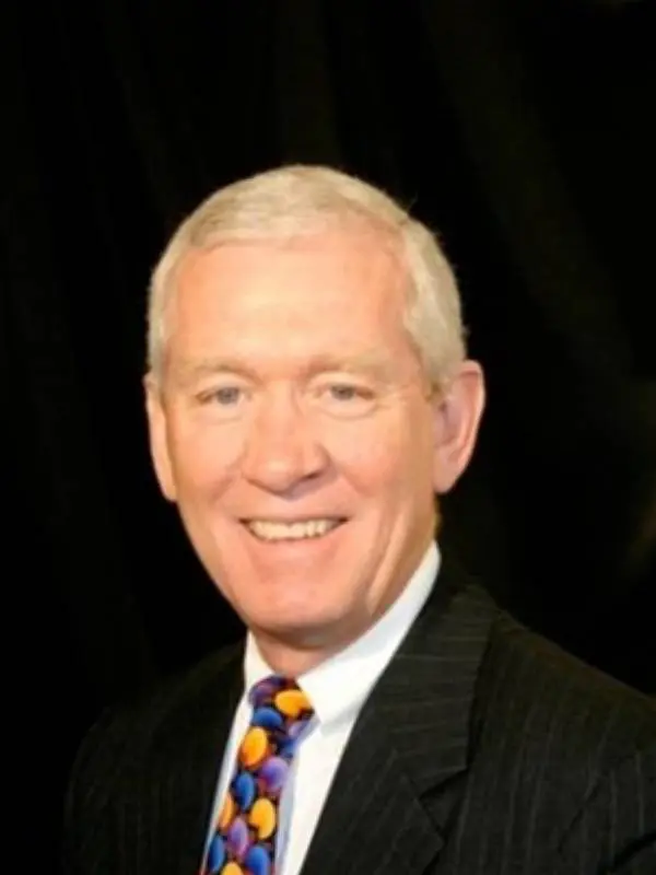 Smiling elderly man in a suit and tie against a black background.
