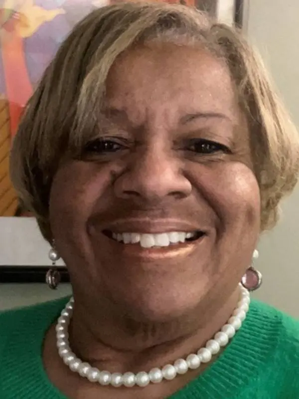 Smiling woman with short blonde hair and pearl necklace.