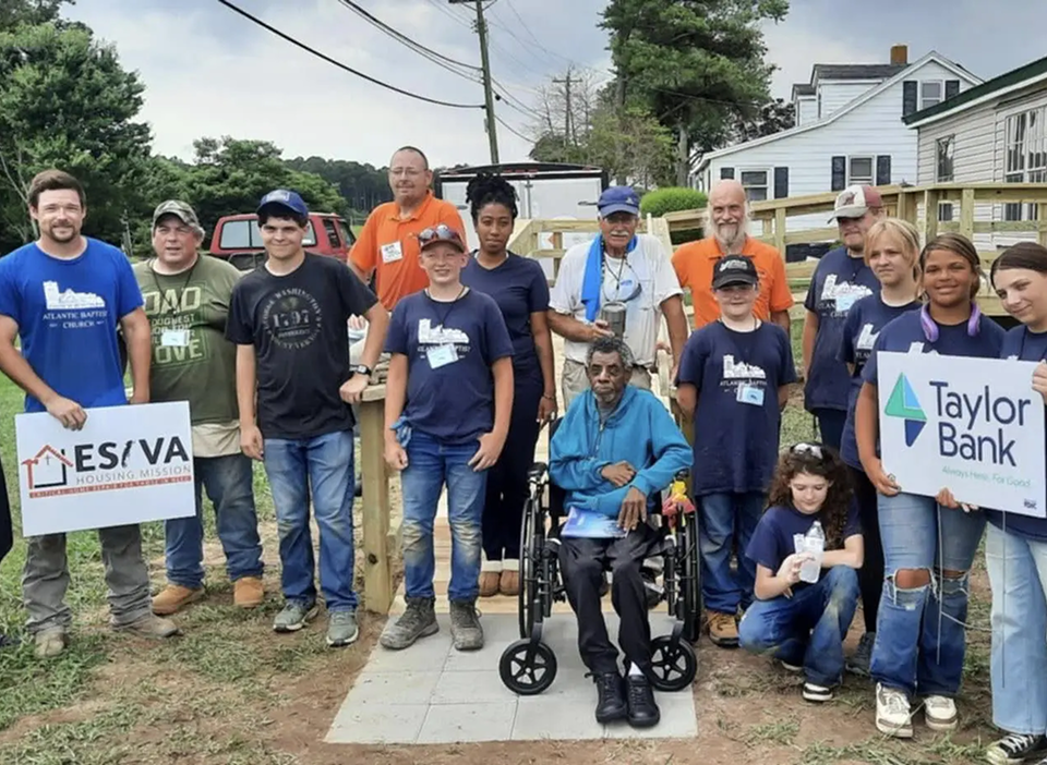 A diverse group of people posing outdoors with signs and a wheelchair.