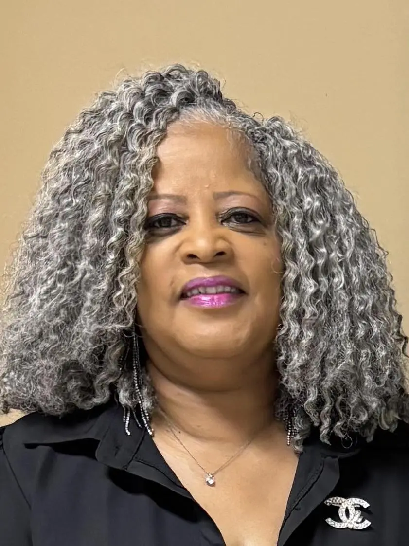 Portrait of a smiling woman with curly gray hair and purple lipstick.