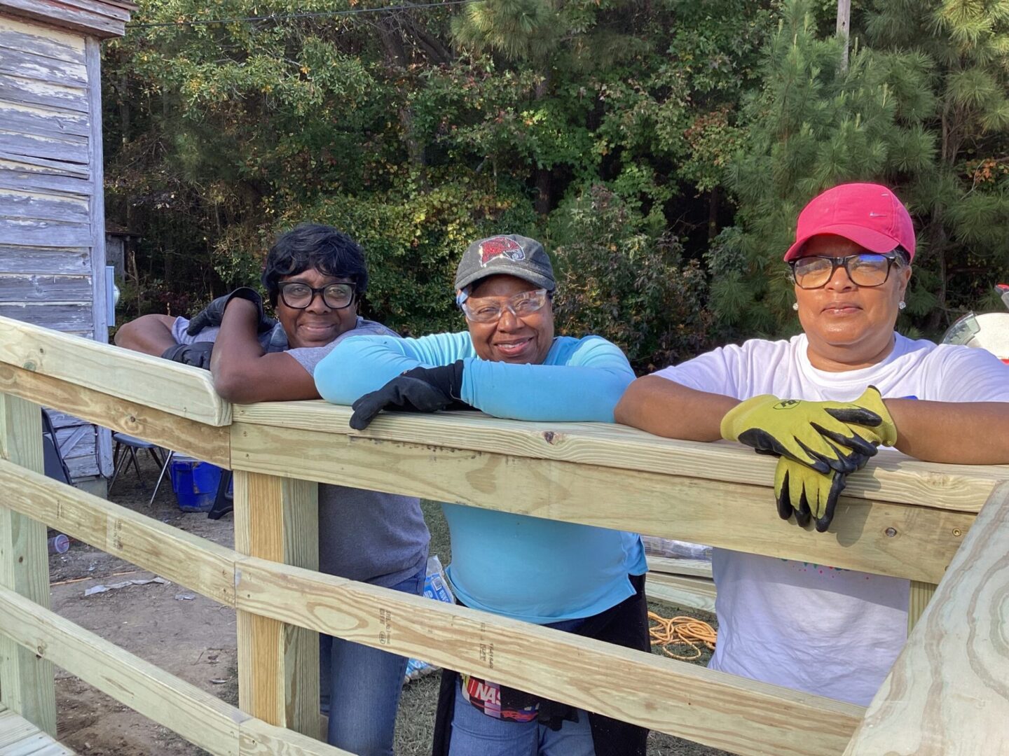 Three people resting on a wooden railing outdoors.