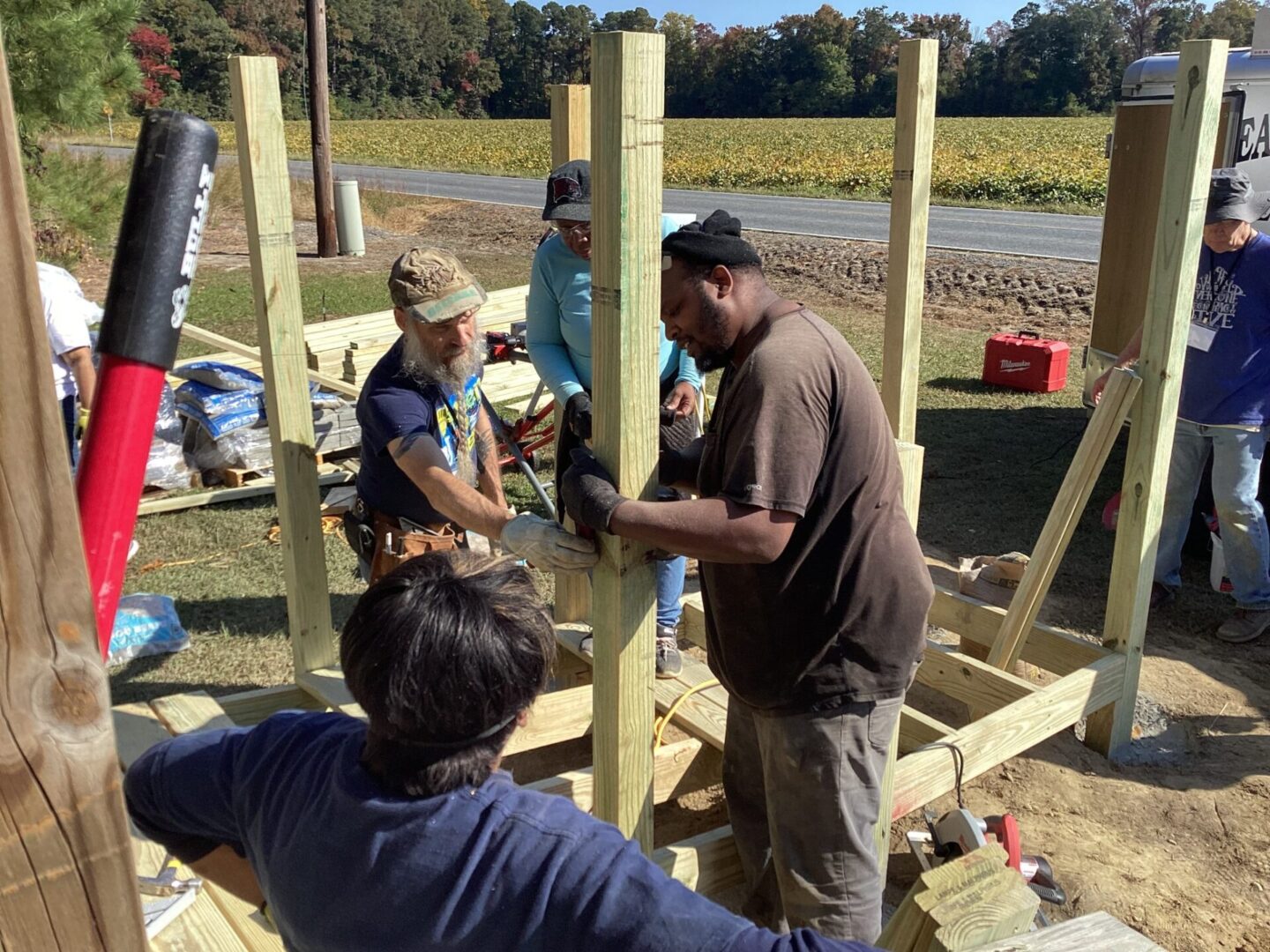 Three people building a wooden structure outdoors on a sunny day.