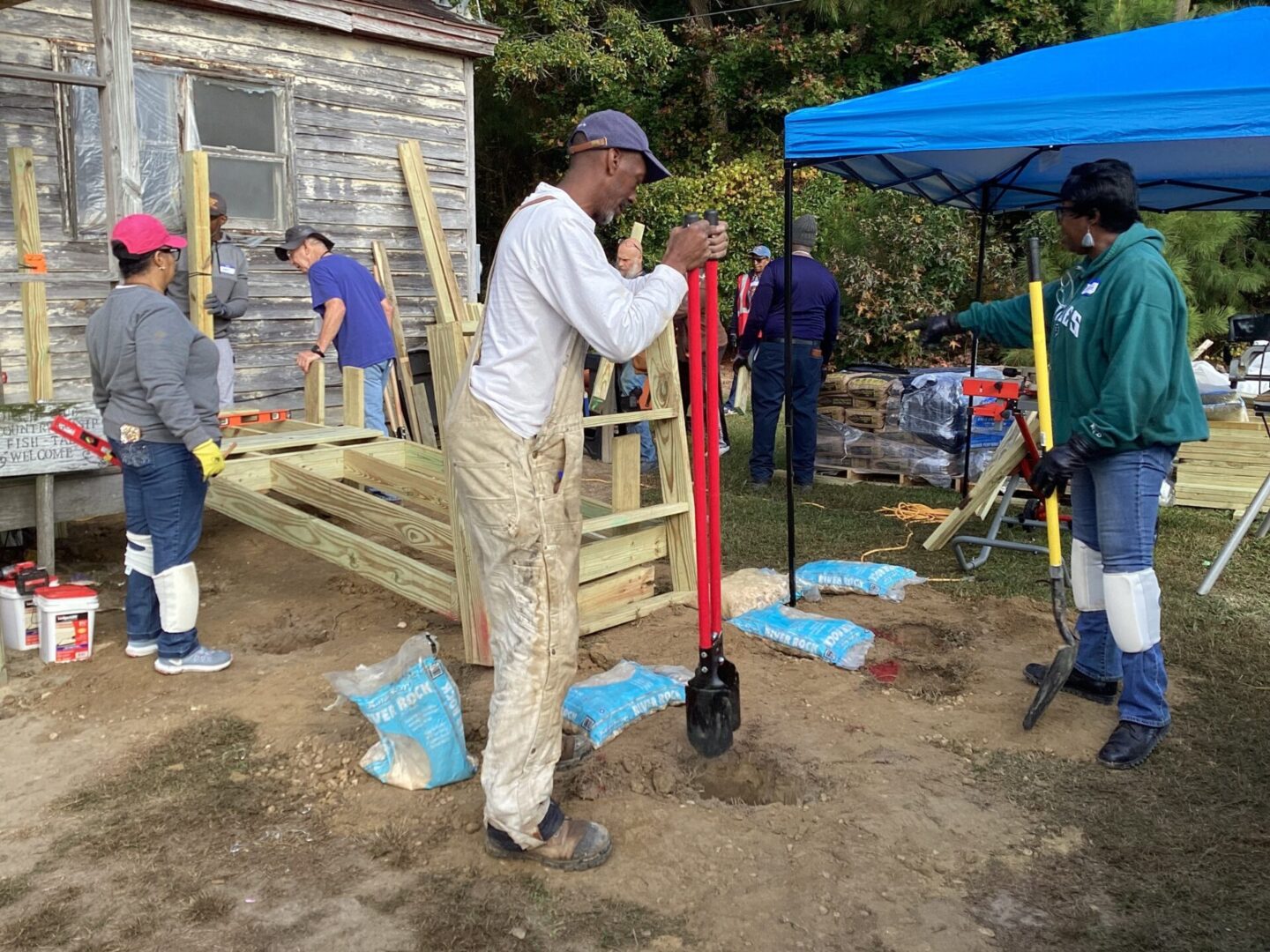 Man in overalls using a manual pallet jack near a wooden structure under construction.