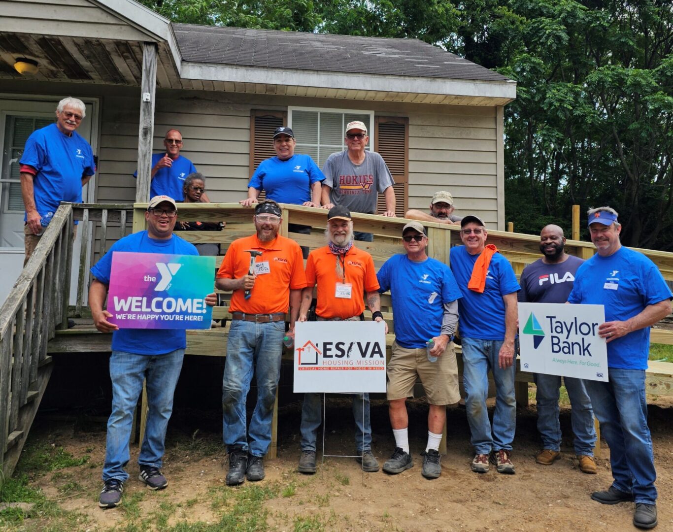 Group of construction workers holding welcome and sponsor signs outdoors.