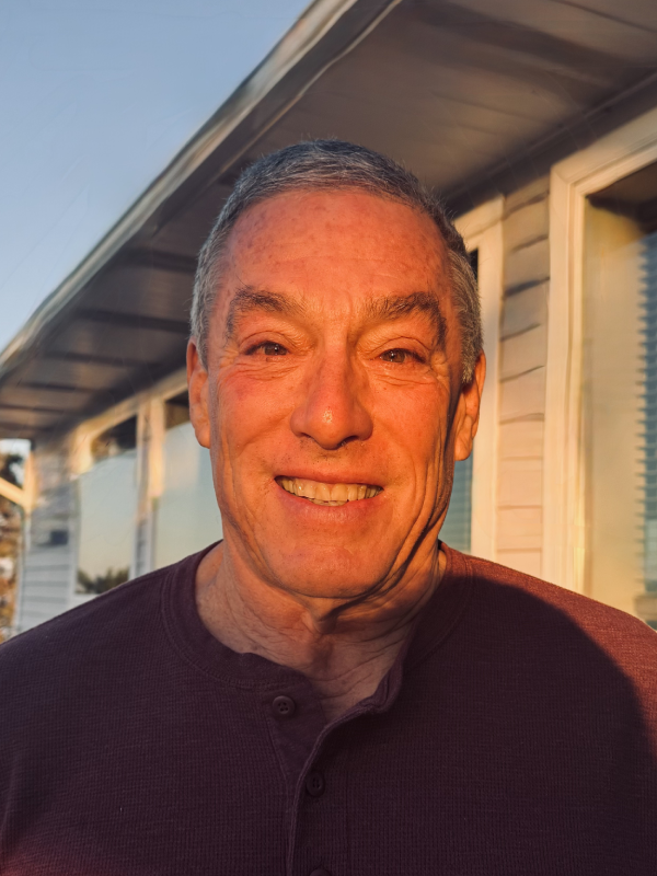 A smiling man outdoors near a building at sunset.