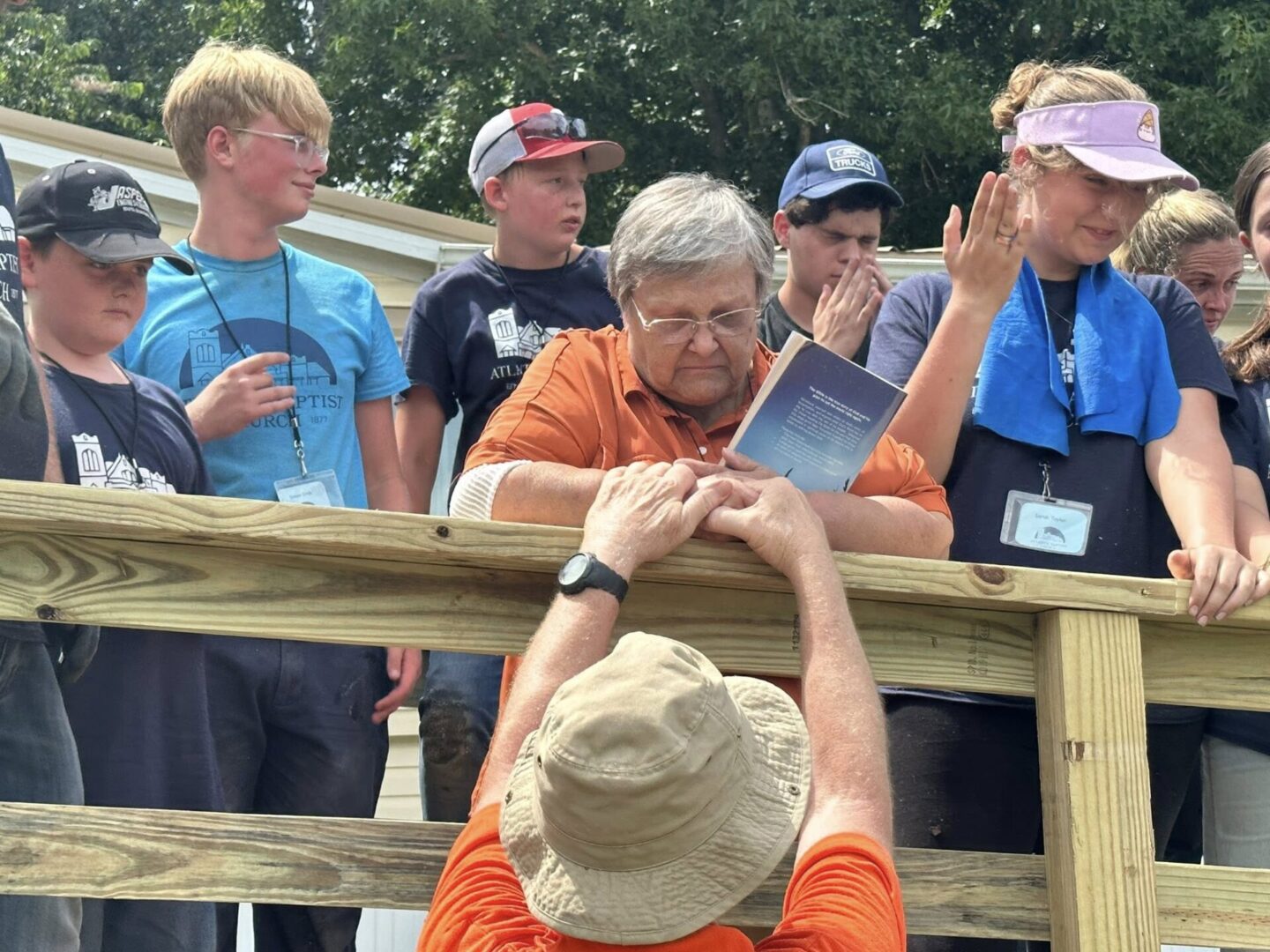 A group of people engaging in an outdoor conversation on a wooden deck.