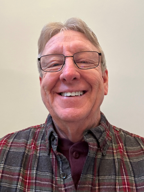 Smiling older man wearing glasses and a plaid shirt.