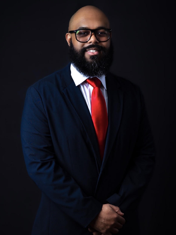 Man in a suit with a red tie smiling against a black background.