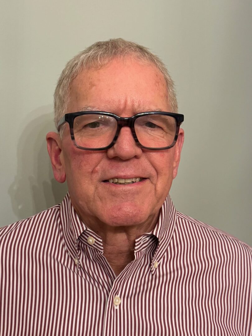 Smiling elderly man wearing glasses and a striped shirt.