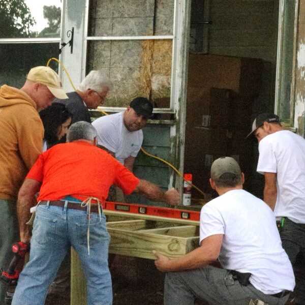 Group of men working together to move a large wooden object.